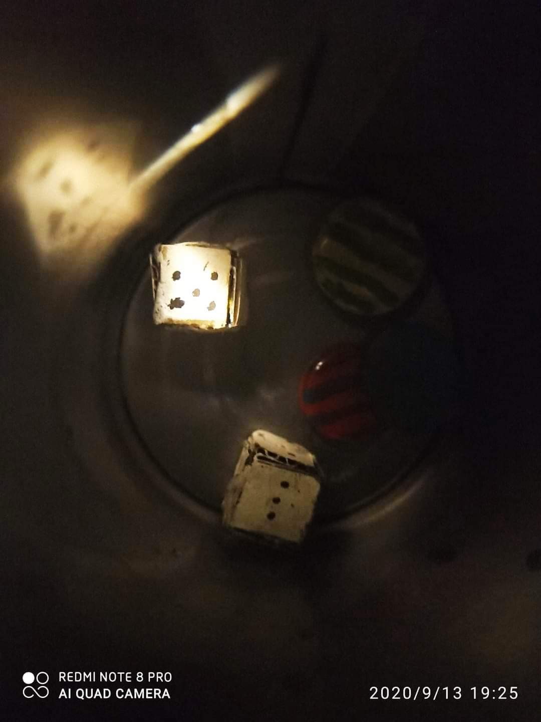 Handmade cardboard dice in a glass, photographed in low light — glowing faces lit dramatically from below