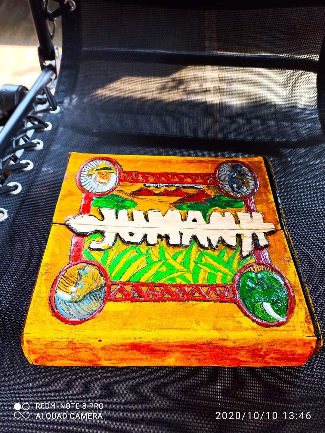 Handmade Jumanji board game cover recreated in cardboard — painted in orange, red, gold and green with raised "JUMANJI" lettering and animal medallions at corners