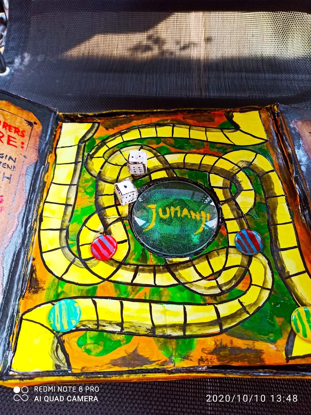 Top-down view of the Jumanji game board mid-play — handmade cardboard dice, coloured marble playing pieces on the spiral track