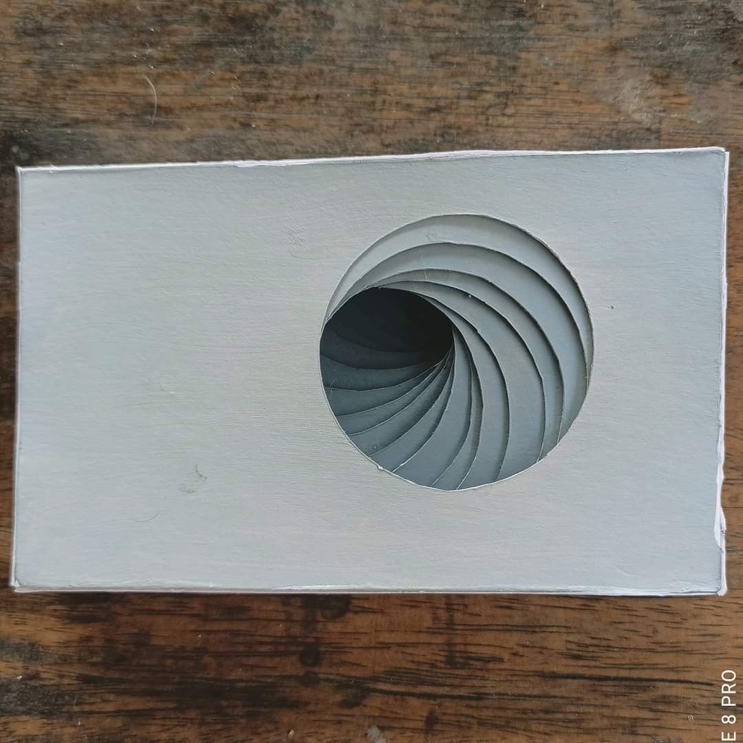 White painted cardboard panel with a spiral vortex cut into a circular opening — layered fins creating a tunnel effect, monochrome grey